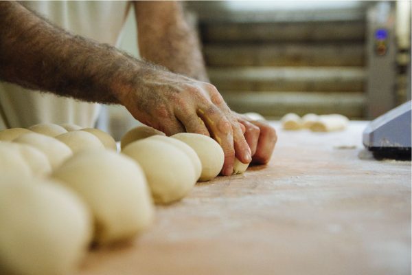 An image of a man's hands making bread rolls on a floured table