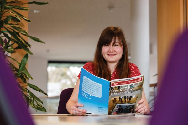 Female student reading Business Cornwall magazine in an office