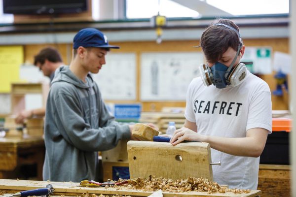 Student treating wood in workshop wearing breathing mask