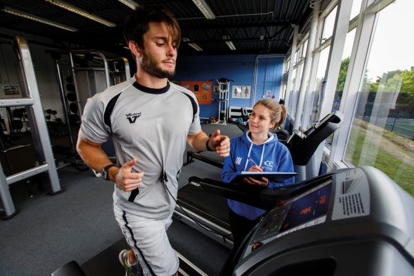 A male student runs on a treadmill whilst another student records his time and heart rate.