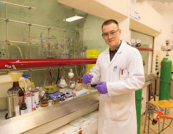 Science student standing in a lab holding a beaker.