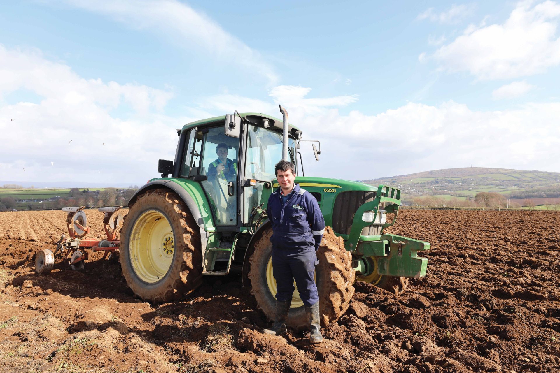 Student standing in front of a tractor in a ploughed field.