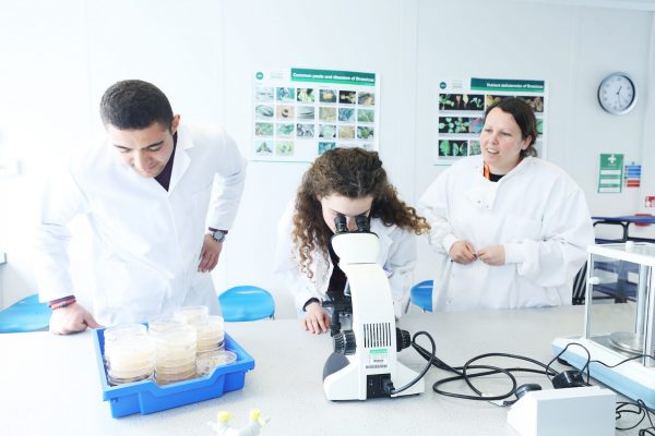 three students looking at samples through microscope in the plant science lab at The Eden Project