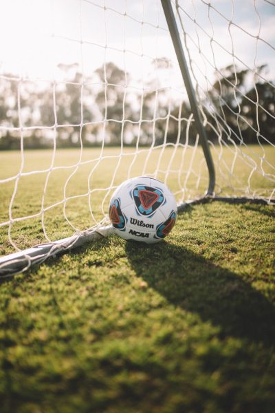 Football in a goal on grassy pitch