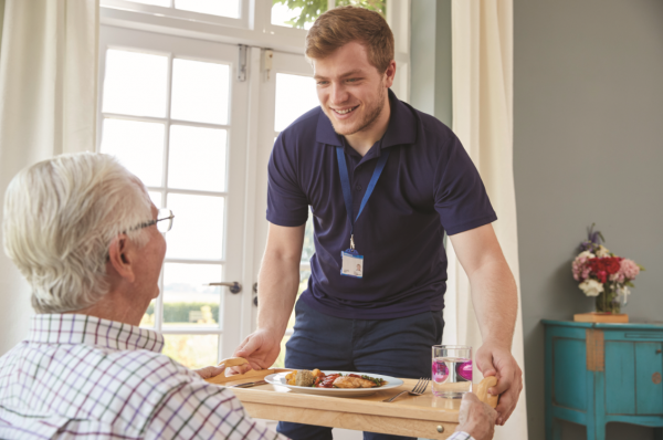 Male care worker serving food to an older adult