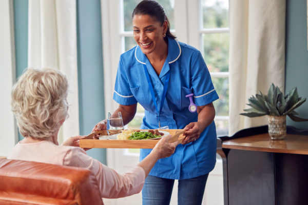 A care assistant handing a tray of food to an elderly patient