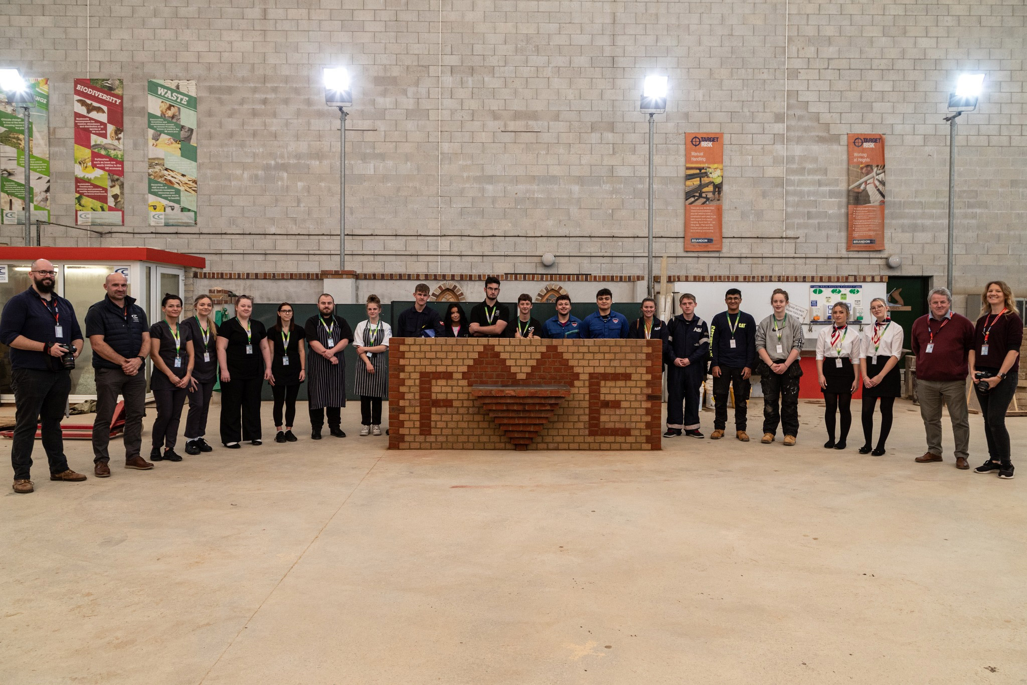 Students standing around a brick wall with the We Love Our Colleges logo