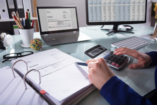 Accountant in front of invoices and laptop screen holding a calculator