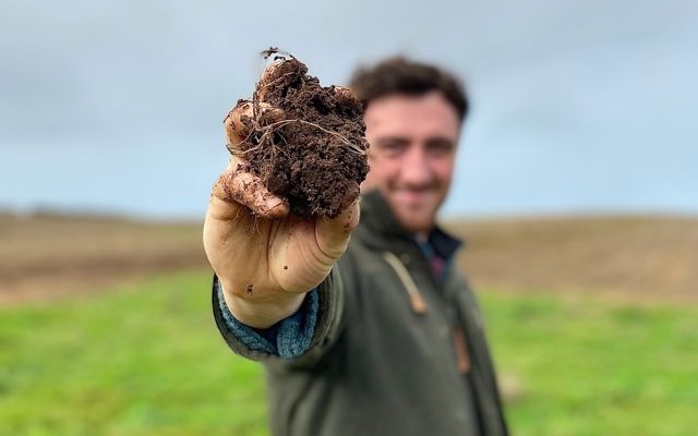 Man that's stretching his arm to the camera, while showing soil in his hand