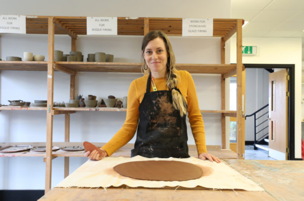 Smiling student looking at the camera, while starting to work on her ceramic structure.