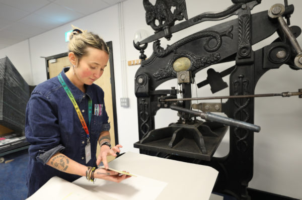 A student putting down her design on a paper placed on top of the lino print machine.
